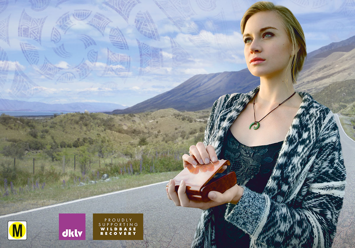 Jade holding a small wooden box on a road through New Zealand's mountains